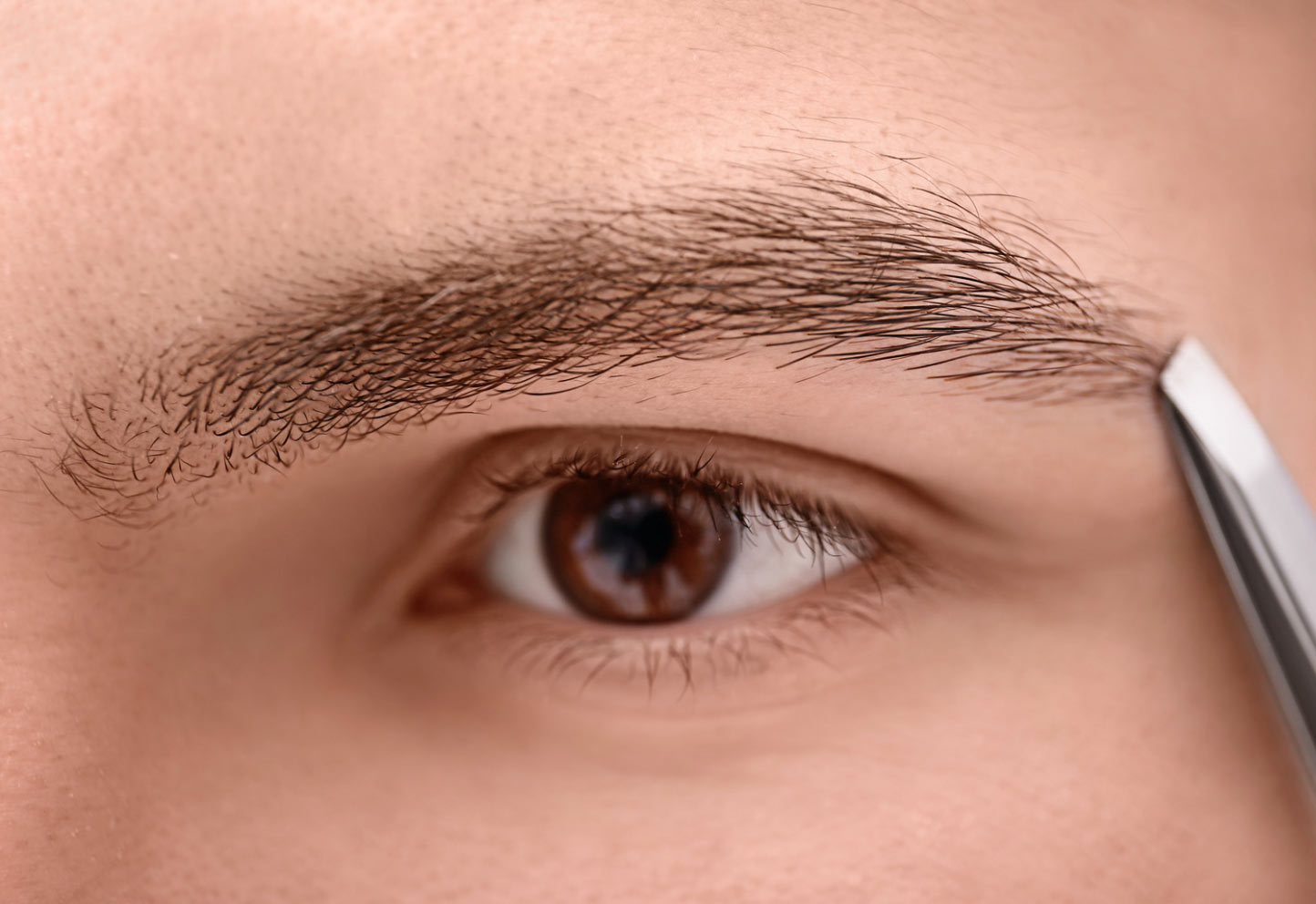 Men's Eyebrow Grooming - Eyelashes by Dina in Houston, TX. Close-up of a person using tweezers to groom their right eyebrow.