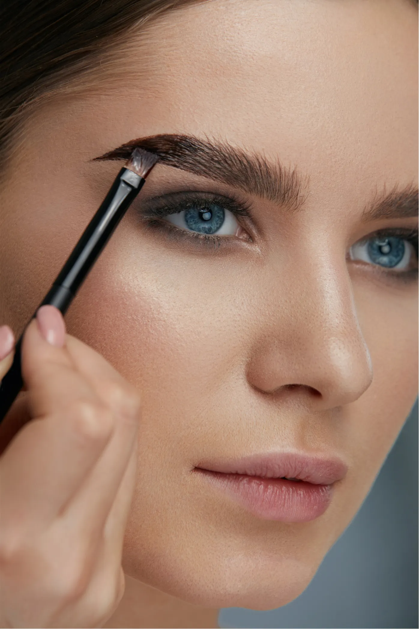 A person fills in their eyebrow with a brush, focusing on detailed makeup application.