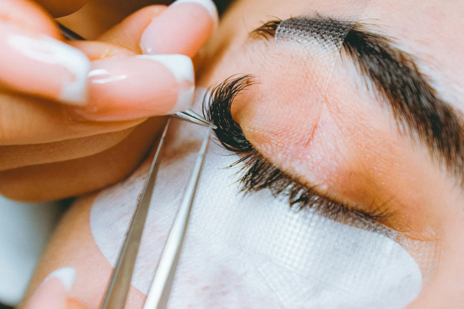 Close-up of eyelash extensions being applied with tweezers to a person's closed eye.